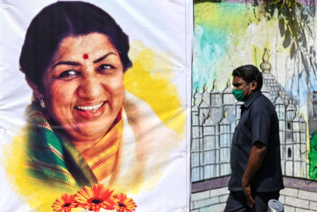 Seorang pejalan kaki berjalan melewati poster dengan gambar mendiang penyanyi Bollywood, Lata Mangeshkar, yang dipasang untuk mengenangnya, di Mumbai, India, Senin (7/2/2022), sehari setelah kematiannya.