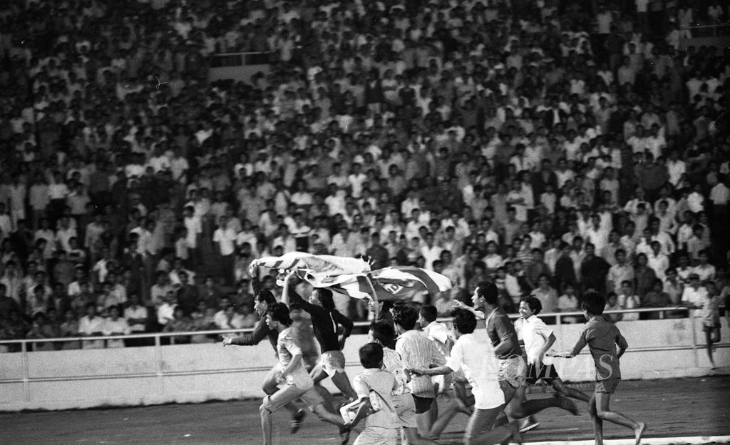 Pemain Persija melakukan victory lap dengan menjunjung bendera DKI Jaya di atas kepala setelah Persija tampil sebagai juara kompetisi PSSI 1973, sementara suporter cilik ikut memeriahkan. Tampak antara lain (dari depan) kiper cadangan A Rake, Yudo Hadiyanto dan di belakang adalah Widodo (11/12/1973).