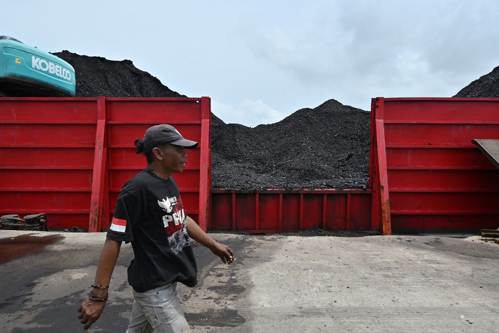 Seorang pria melintas di depan tumpukan batu bara di pelabuhan KCN Marunda, Jakarta, Senin (17/1/2022).