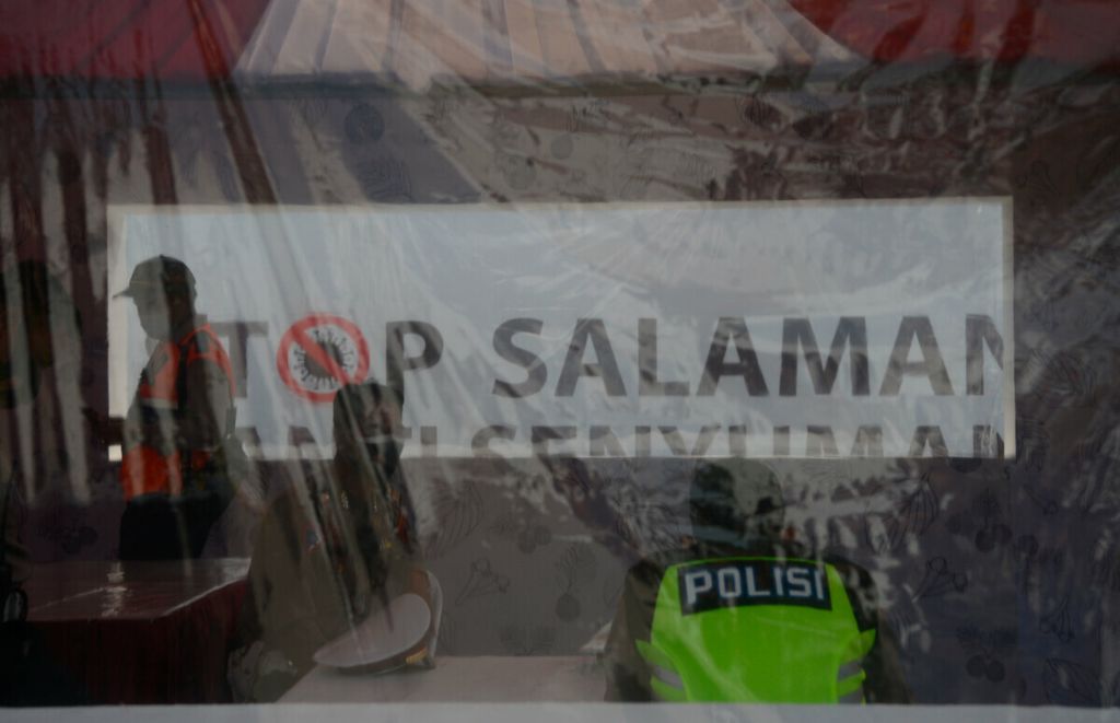 Petugas berada di dalam pos penjagaan dengan latar belakang sebuah tulisan “Stop Salaman” di gerbang tol Kalikangkung, Kota Semarang, Jawa Tengah, Selasa (3/4/2021). Pemerintah mengeluarkan kebijakan pelarangan mudik Lebaran untuk mengantisipasi penyebaran Covid-19 yang masih sebagai ancaman.