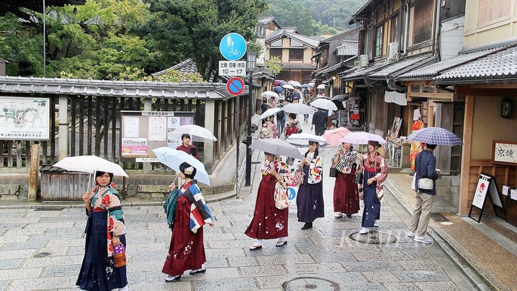Para turis dalam baju tradisional berjalan di tengah hujan di permukiman kuno yang dilestarikan di Jalan Ninenzaka di Distrik Gion yang dikenal sebagai salah satu pusat geisha di Kyoto, Jepang, Senin (16/10/2017). 