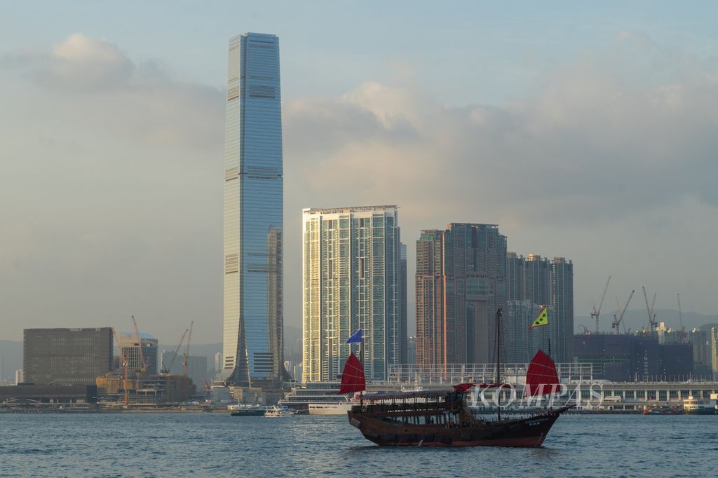 Kapal tradisional <i>junk boat</i> melintas di selat sempit dengan latar belakang gedung-gedung pencakar langit di Hong Kong, Rabu (22/11/2023).