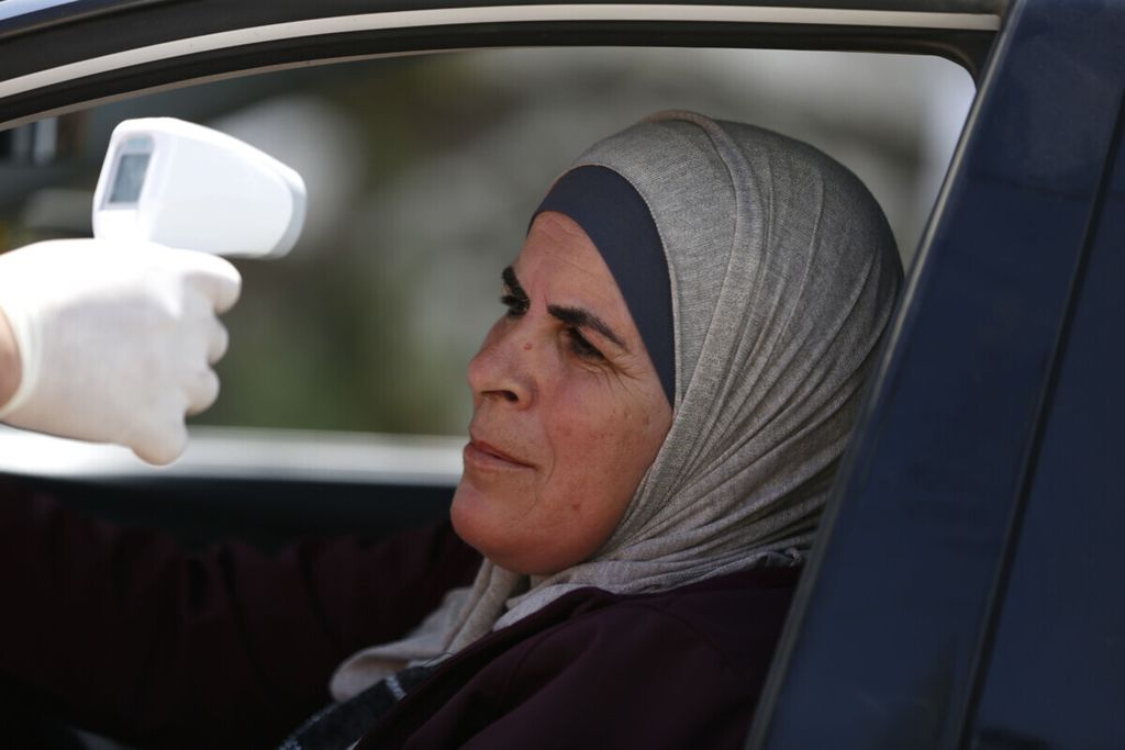 A Palestinian volunteer measures the temperature of a woman entering the village of Ain Yabrud near Ramallah, as civilians deployed along rural roads in the occupied West Bank to enforce coronavirus controls amid the COVID-19 pandemic, on April 6 , 2020. 