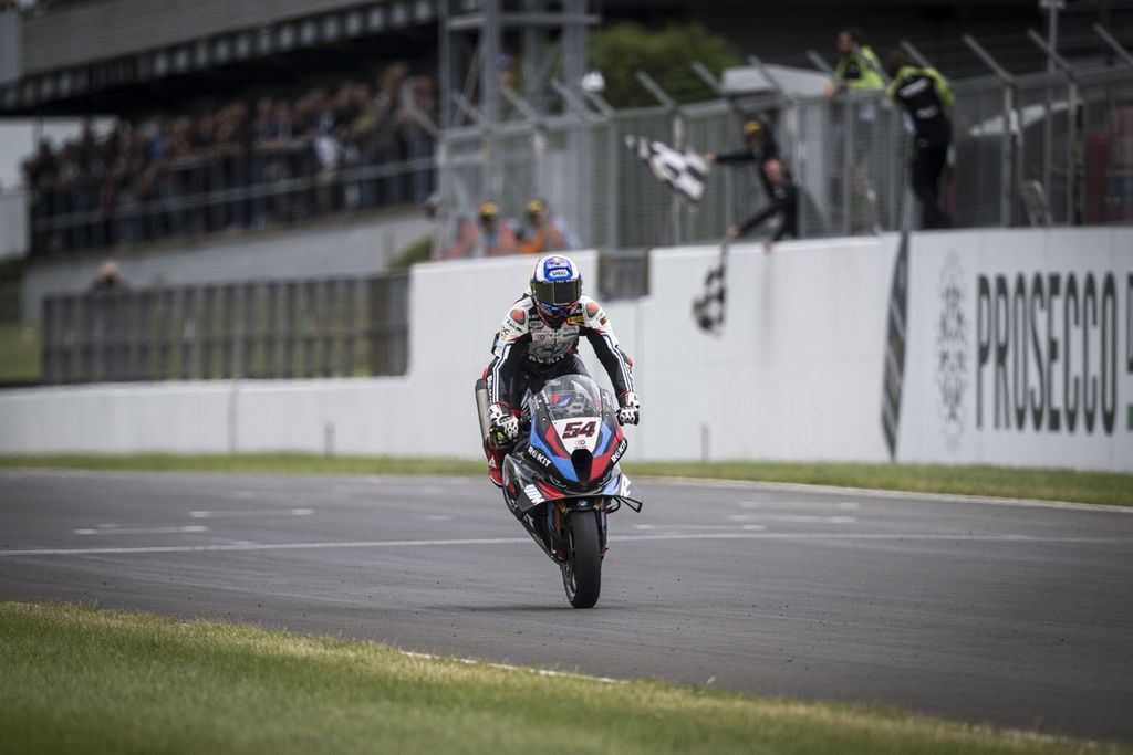 Pebalap tim Rokit BMW Motorrad WorldSBK, Toprak Razgatlioglu, melakukan<i> stoppie </i>saat merayakan kemenangan balapan 2 Superbike seri Inggris di Sirkuit Donington Park, Sabtu (13/7/2024). Razgatlioglu meraih tiga kemenangan di Donington Park, mengulang <i>hattrick</i> di Misano. Dia kini memuncaki klasemen dengan 241 poin.