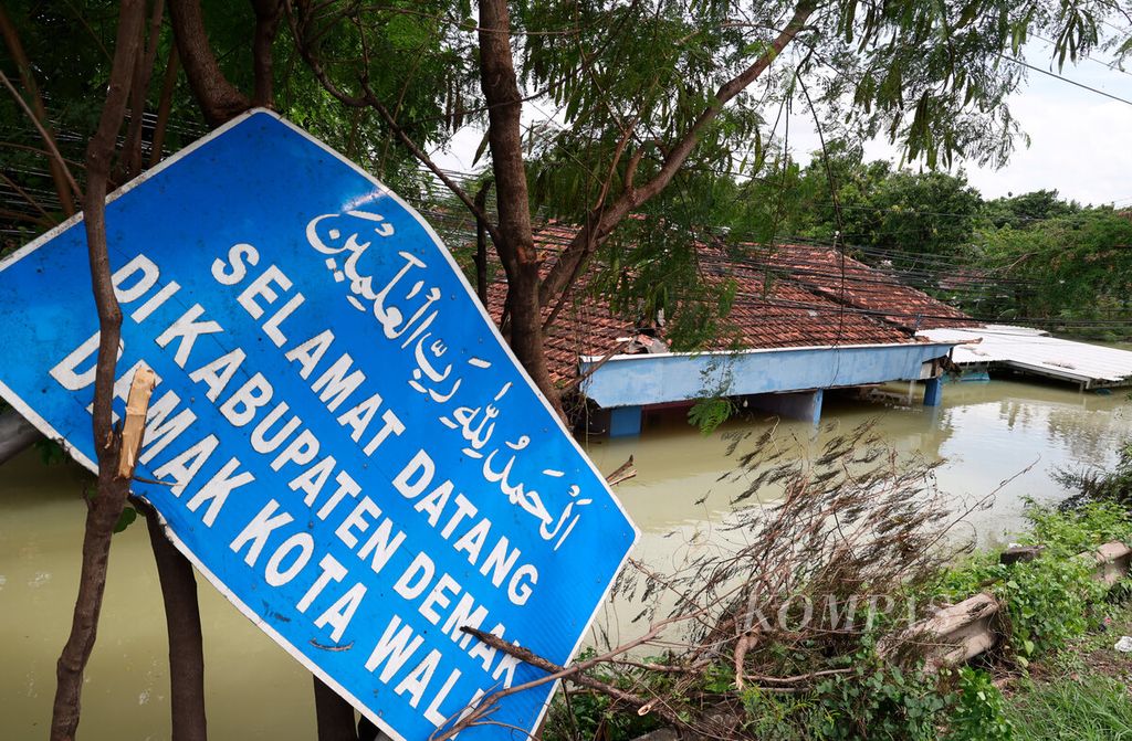 Plang perbatasan wilayah dengan latar belakang rumah warga yang terendam banjir di Desa Ketanjung, Kecamatan Karanganyar, Kabupaten Demak, Jawa Tengah, Minggu (17/3/2024). 