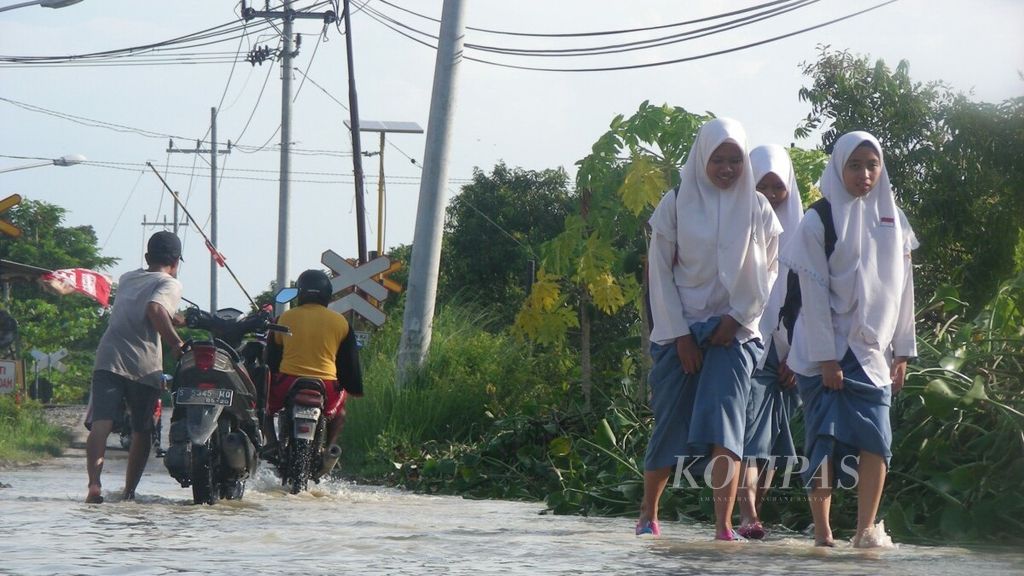Siswi SLTA berjalan menembus banjir di akses menuju Madrasah Aliyah Negeri Babat, Lamongan, Jawa Timur, Selasa (19/3/2019).