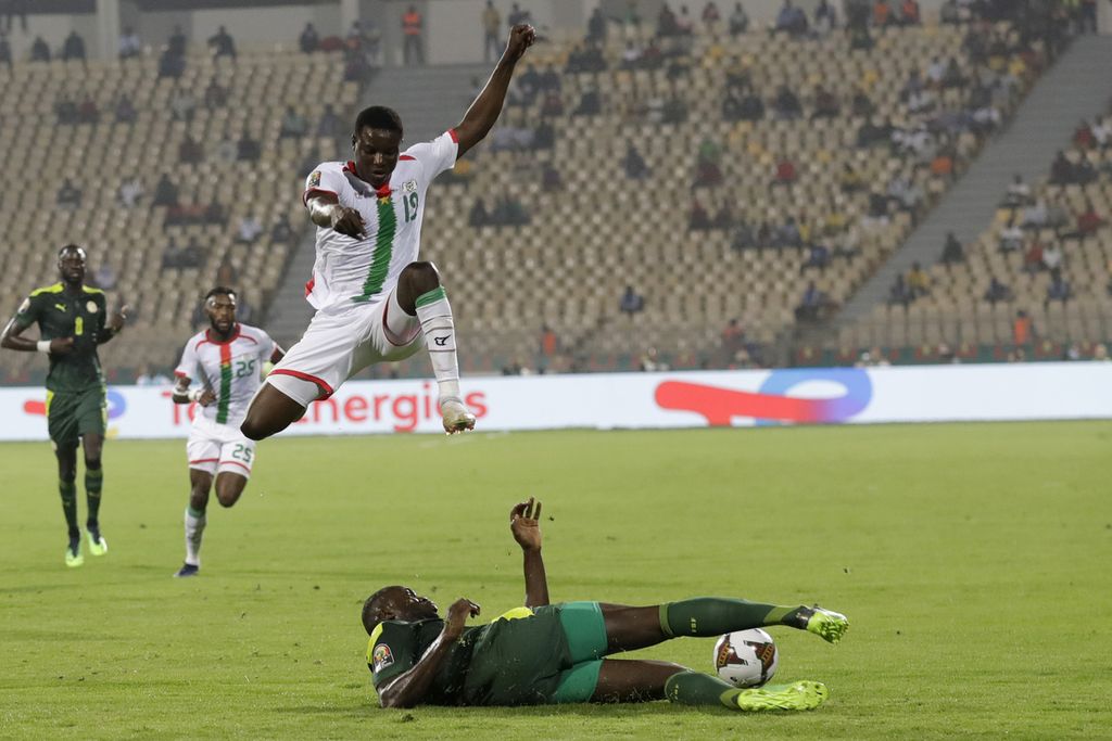 Penyerang Burkina Faso, Hassane Bande (atas), menghindari tekel bek Senegal, Kalidou Koulibaly, dalam babak semifinal Piala Afrika 2021 di Stadion Ahmadou-Ahidjo, Younde, Kamerun, Kamis (3/2/2022) dini hari WIB. Burkina Faso memperkecil ketinggalan melalui gol Ibrahim Blati Toure pada menit ke-82.