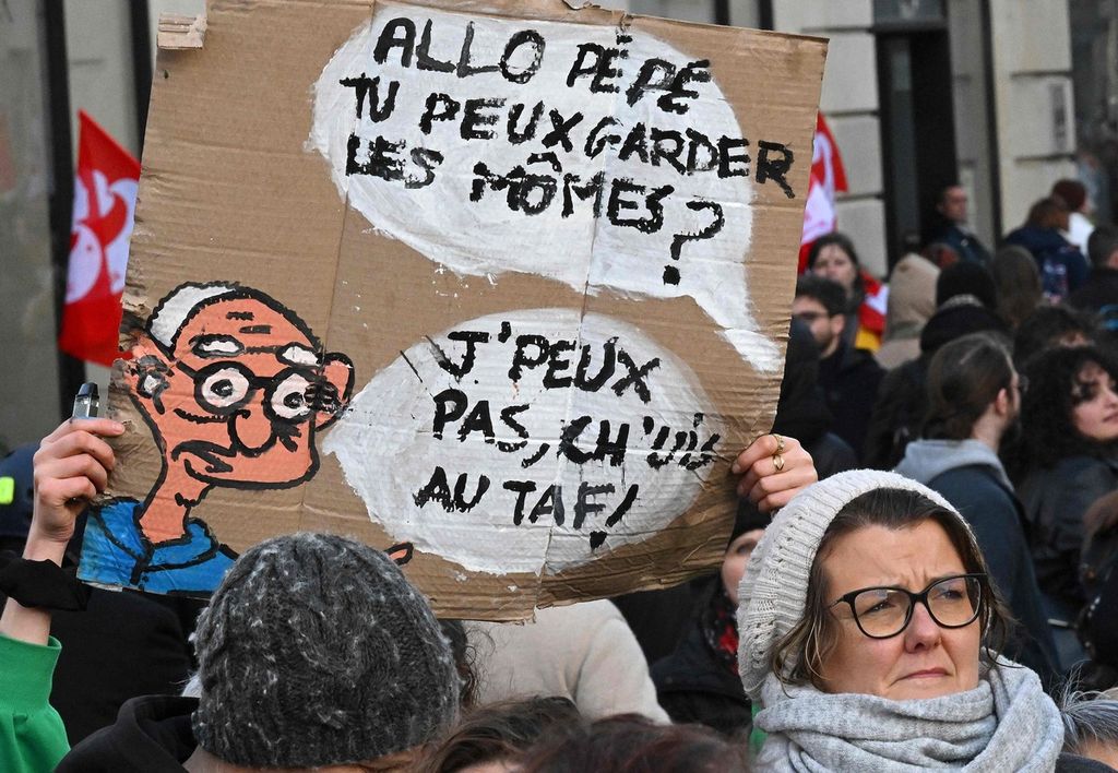Pengunjuk rasa memegang papan yang bertulis "Halo, Kakek. Bisa bantu menjaga anak-anak? Tidak bisa. Aku sedang bekerja." di Lille, Perancis bagian utara pada tanggal 31 Januari 2023. Masyarakat menolak Undang-Undang Reformasi Usia Pensiun yang didorong oleh Presiden Emmanuel Macron.