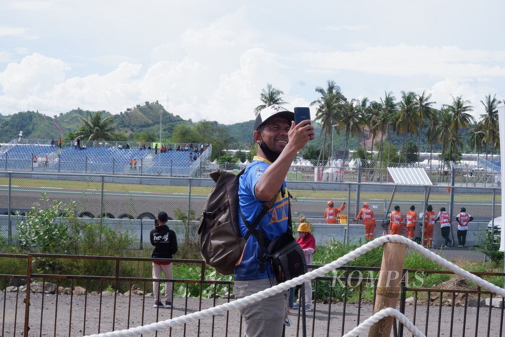 Mario Manuhutu (38) asal Timika, Papua, berfoto dari area penonton kelas <i>general admission </i>atau festival dengan latar belakang aksi pebalap yang tampil dalam rangkain MotoGP di Sirkuit Internasional Jalan Raya Pertamina Mandalika, Kuta, Pujut, Lombok Tengah, Nusa Tenggara Barat, Jumat (18/3/2022) pagi. Tidak hanya dari dalam, penonton yang datang ke Sirkuit Mandalika untuk menonton rangkaian MotoGP juga dari berbagai wilayah di Indonesia.