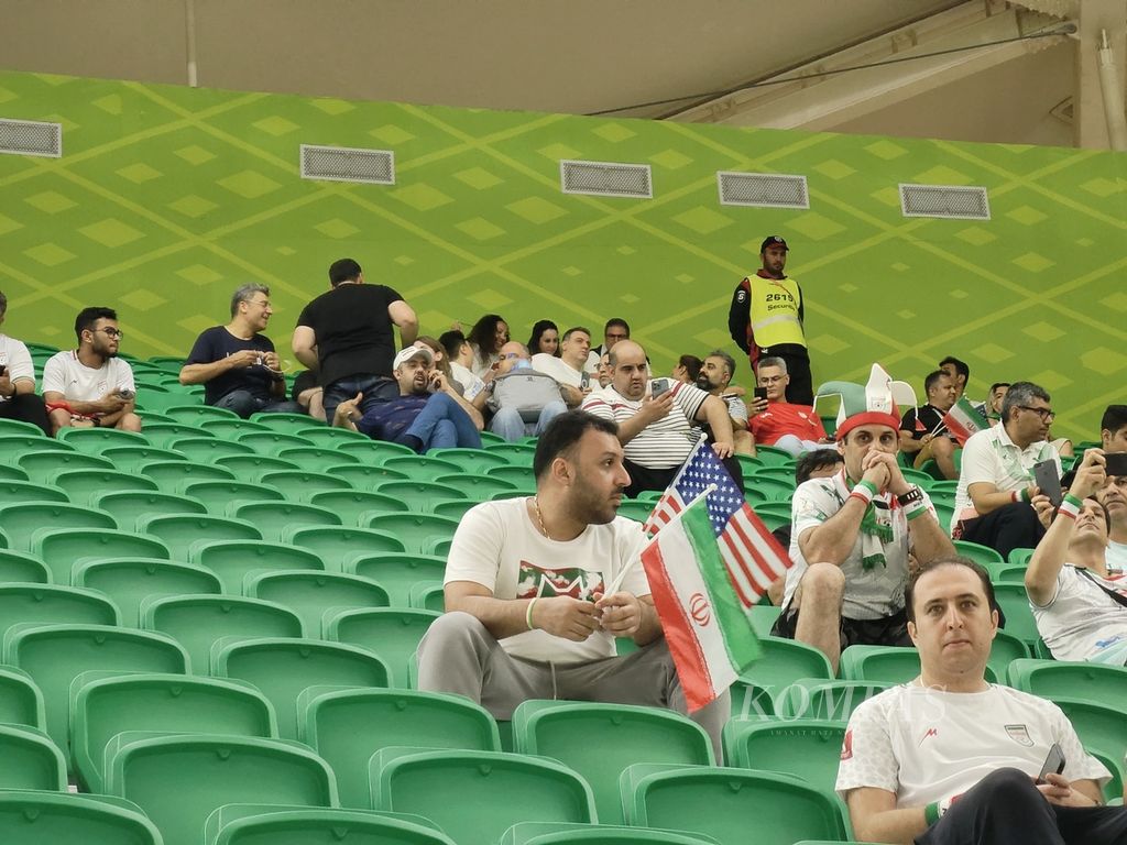 Seorang pendukung Iran memegang bendera Iran dan Amerika Serikat ketika menyaksikan laga kedua negara, Rabu (30/11/2022), di Stadion Al Thumama, Doha. Meski kedua negara berseteru, pendukung Iran dengan senang hati mengibarkan bendera AS.