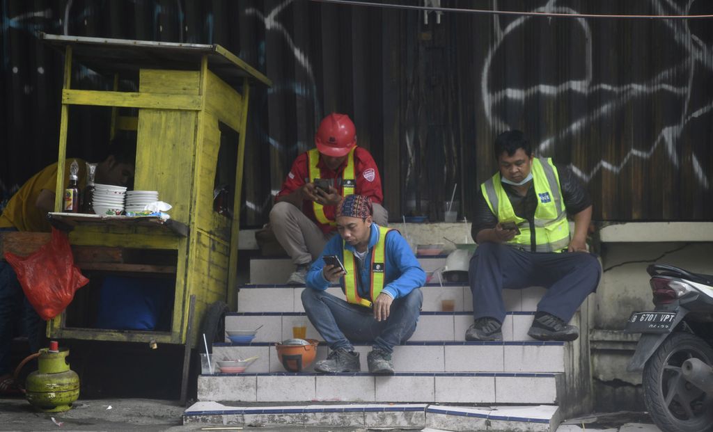 Sejumlah pekerja proyek sibuk melihat gawai masing-masing saat jam istirahat makan siang di salah satu lokasi pembangunan gedung bertingkat di Jakarta, Kamis (17/2/2022). Pemerintah diharapkan dapat menunda Permenaker Nomor 2 Tahun 2022 tentang Tata Cara dan Persyaratan Pembayaran Manfaat Jaminan Hari Tua untuk mengevaluasi kesiapan program Jaminan Kehilangan Pekerjaan (JKP) sebagai pengganti Jaminan Hari Tua (JHT). 