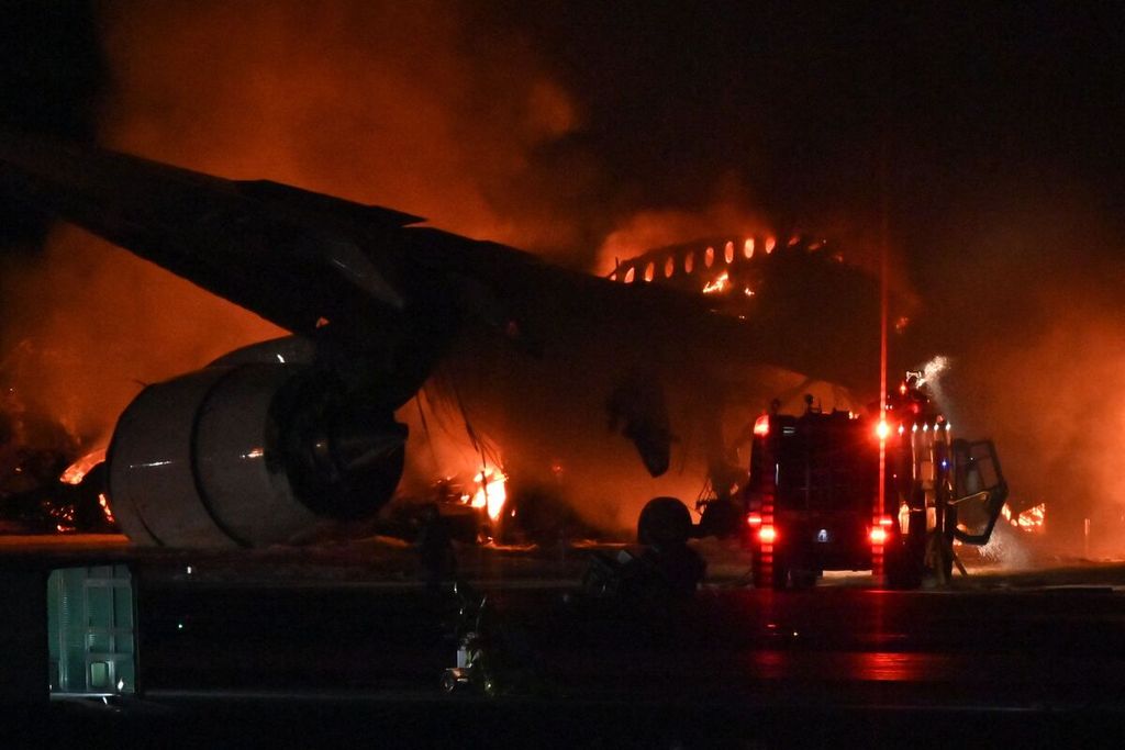 Petugas pemadam kebakaran tengah berupaya memadamkan api yang melahap Airbus A350 yang dioperasikan Japan Airlines. Pesawat tersebut terbakar di landasan pacu Bandara Haneda, Jepang, setelah bertabrakan dengan pesawat Penjaga Pantai Jepang pada Selasa (2/1/2023).