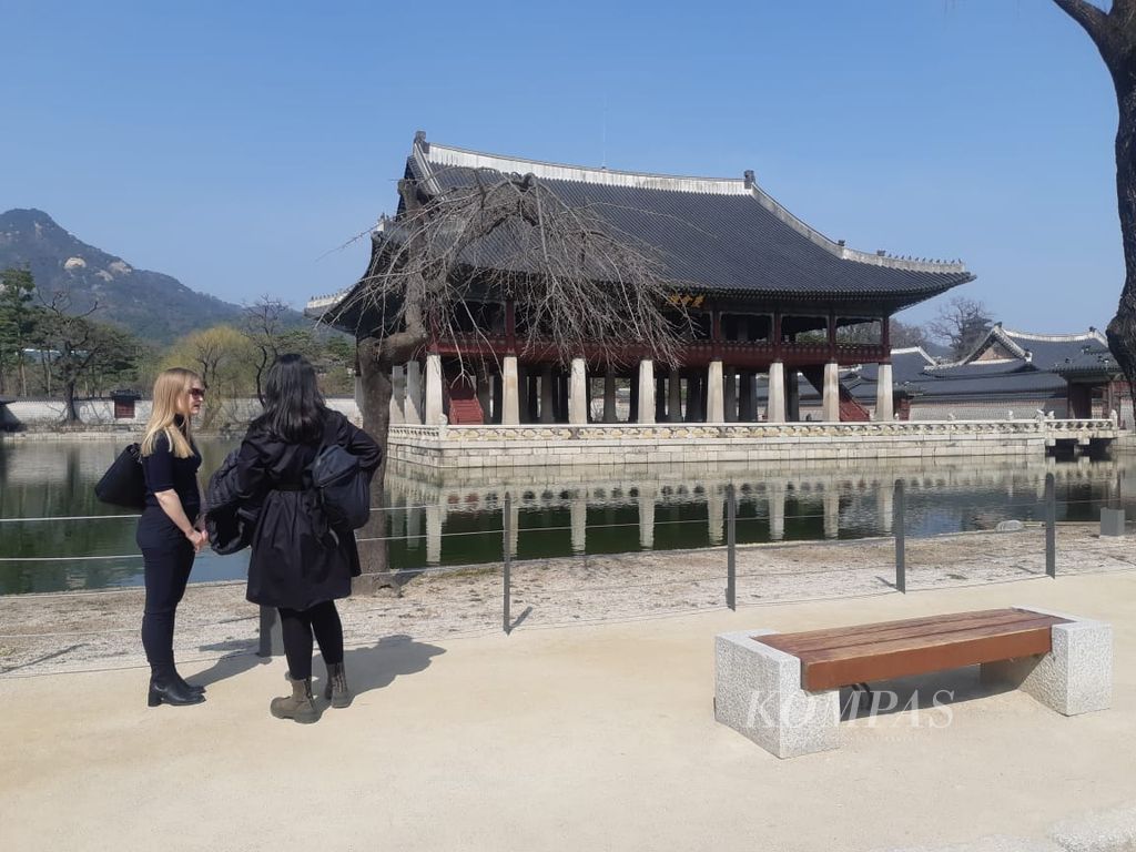 Turis mancanegara berbincang sambil menatap Paviliun Gyeonghoeru di Istana Gyeongbokgung, Seoul, Korea Selatan, Maret 2023.
