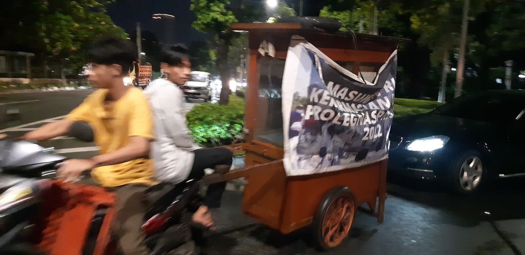 Pedagang sate taichan membawa gerobak jualannya dengan sepeda motor ke Jalan Tentara Pelajar, Gelora, Jakarta Pusat, Jumat (10/2/2023). Kegiatan ini baru mereka lakukan di atas pukul 22.00 setelah petugas satpol PP yang biasa berjaga di jalan itu pergi.