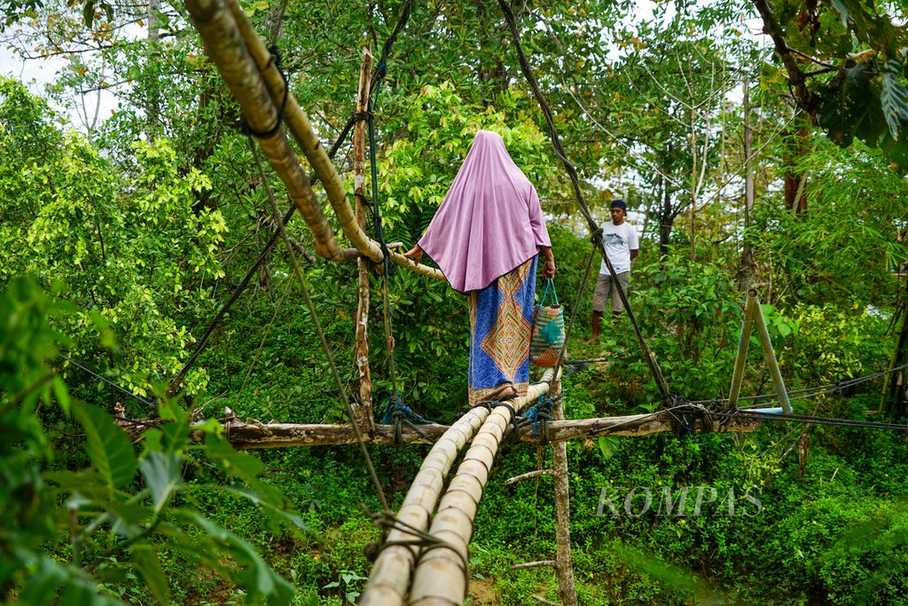 Lawia (50) dan anaknya melintasi jembatan bambu menuju sawah miliknya di Desa Lalowiu, Rabu (14/9/2022).