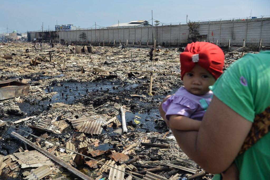 Seorang anak digendong ibunya saat melihat puing-puing sisa kebakaran di kawasan Kampung Nelayan Muara Angke, RT 012, RW 022, Tembok Bolong, Penjaringan, Jakarta Utara, Minggu (23/4/2023). 