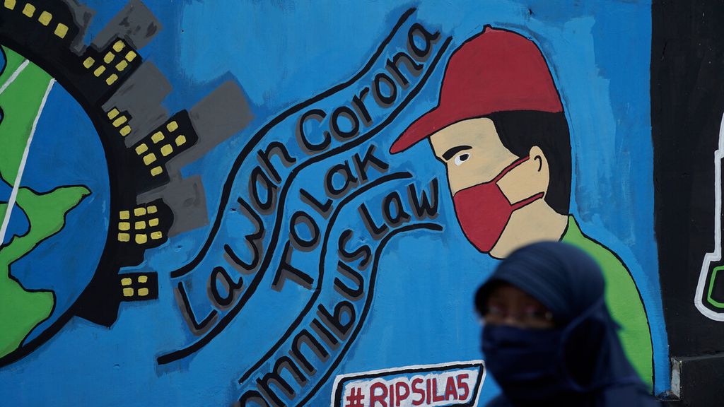Warga melintasi mural Covid-19 dan politik di Jatikramat, Kota Bekasi, Jawa Barat, Senin (26/10/2020). Mural mengkritisi DPR yang mengesahkan UU Cipta Kerja dalam pandemi Covid-19 yang dinilai merugikan rakyat kebanyakan. 