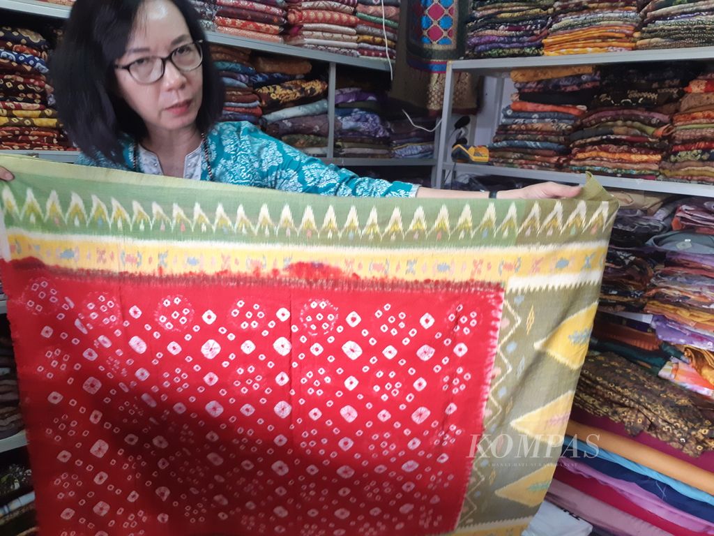 Seorang pedagang kain di Palembang menunjukan kain hasil modifikasi sejumlah motif kain tenun di Palembang, Sabtu (12/3/2022). Modifikasi motif ini dilakukan untuk merangkul generasi muda untuk mencintai kain tenun khas Palembang.