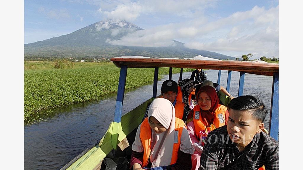 Wisatawan lokal menumpang perahu yang dikelola warga desa menyusuri jalur wisata rawa dengan latar belakang Gunung Kerinci.