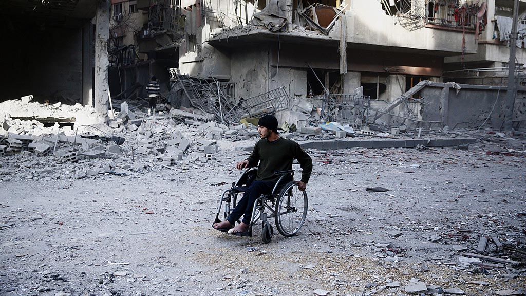 Seorang  warga Suriah tengah melintas dengan kursi rodanya sambil melihat bangunan yang hancur pasca-serangan udara Suriah di Douma, Ghouta timur, Jumat (9/2). 