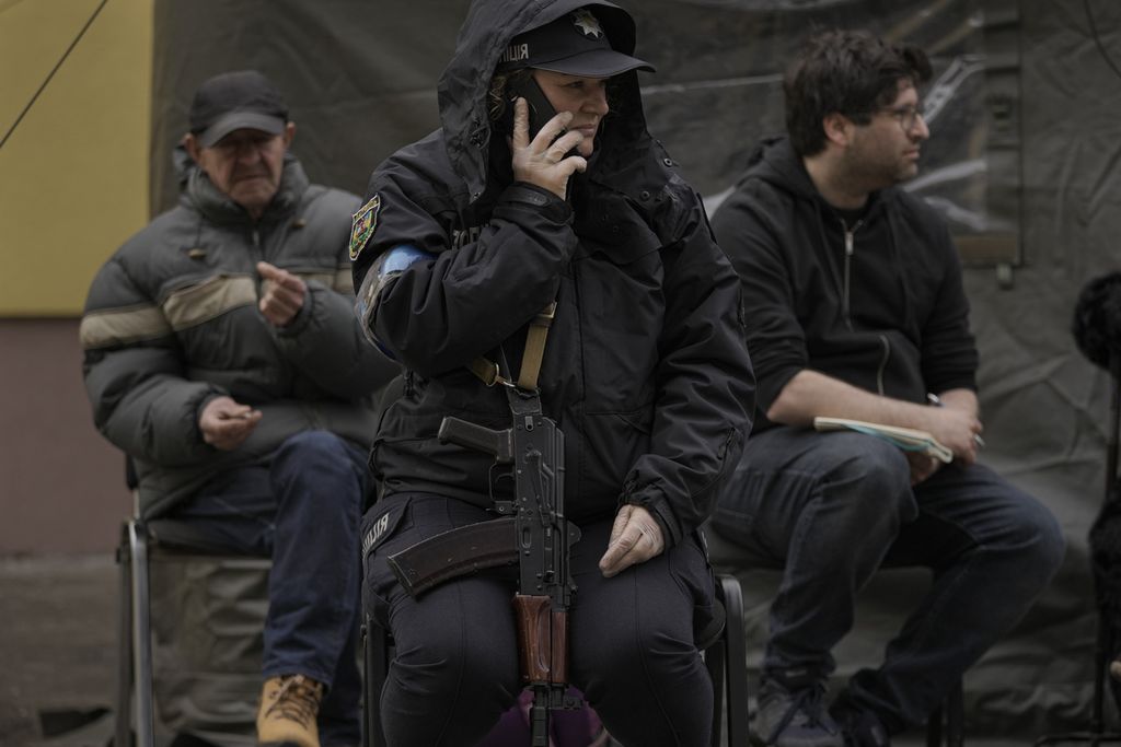 Seorang polisi Ukraina yang mendampingi warga Ukrainan yang dievakuasi dari Irpin tengah berbicara melalui telepon di  pinggrian kota Kiev pada Sabtu (26/3/2022).