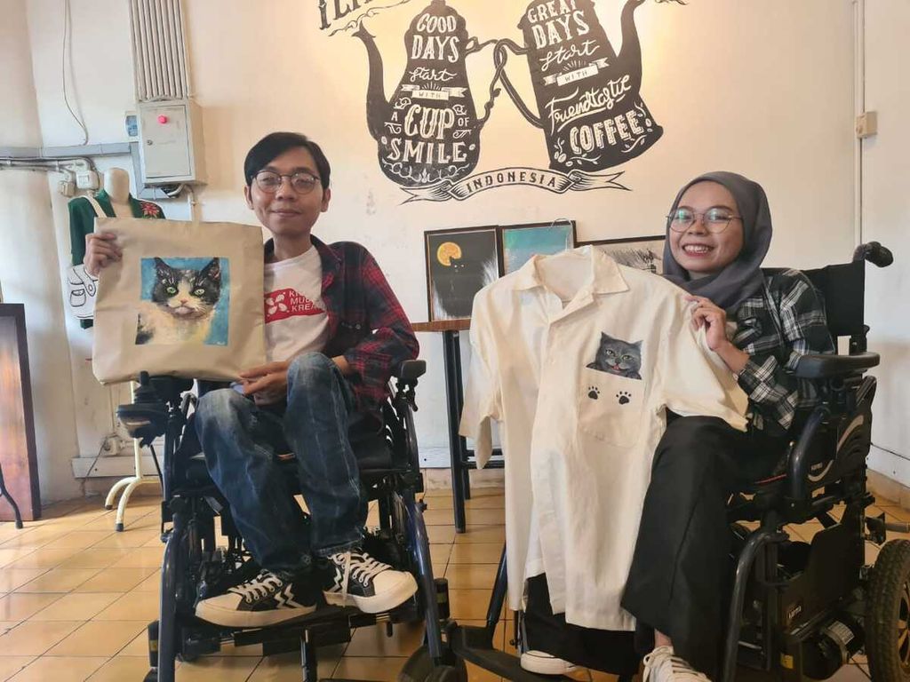Dua pelukis penyandang disabilitas manampilkan dua baju yang dihiasi gambar hasil karya lukis mereka, Jumat (25/11/2022).