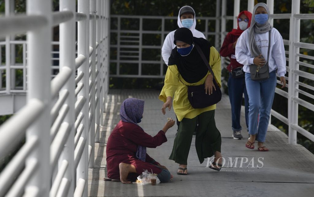 Warga memberikan derma kepada pengemis di jembatan penyeberangan yang terhubung dengan Halte Taman Kota, Jakarta Barat, Senin (1/2/2021). 
