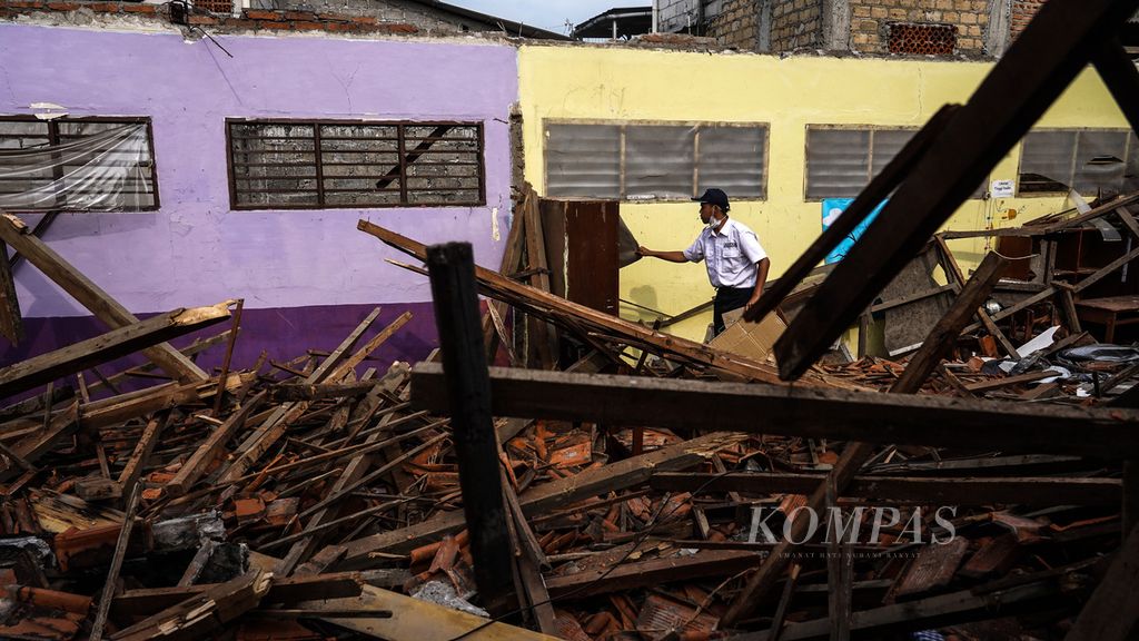 Petugas keamanan berusaha mengambil benda-benda inventaris kelas yang bisa diselamatkan di antara kerusakan dua ruang kelas SD Negeri Ciheuleut 1 dan SD Negeri Ciheulelut 2, Ciheuleut, Kota Bogor, Jawa Barat, akibat roboh atapnya, pada 29 Maret 2022. Robohnya atap kelas dua sekolahan yang berdiri dalam satu lokal bangunan ini terjadi pada 28 Maret 2022. 