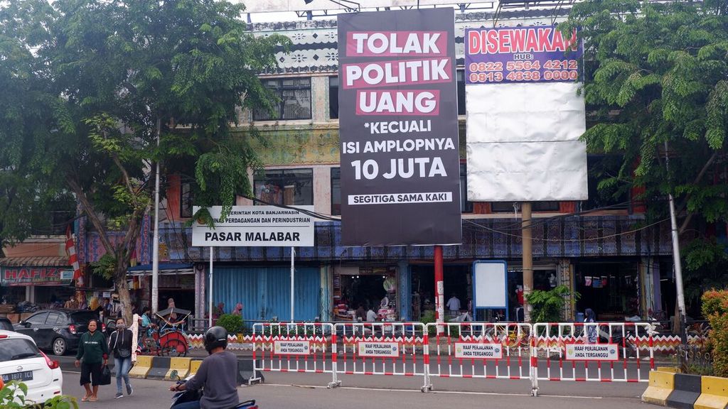 Baliho ajakan untuk menolak politik uang bernada satire terpasang di sudut salah satu pasar di Kota Banjarmasin, Kalimantan Selatan, sehari menjelang pemungutan suara pemilihan kepala daerah serentak 2020, Selasa (8/12/2020). Pada 9 Desember, warga Banjarmasin akan memilih gubernur dan wali kota periode 2021-2024. 