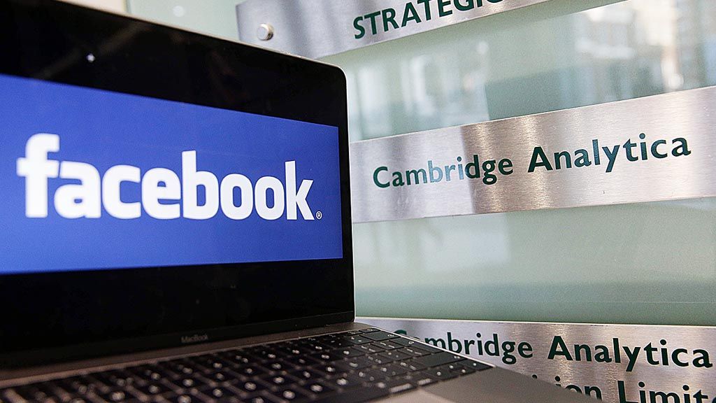 Sebuah laptop memperlihatkan  logo Facebook diletakkan di samping logo Cambridge Analytica di depan pintu masuk kantor Cambridge Analytica di London, Rabu (21/3).
