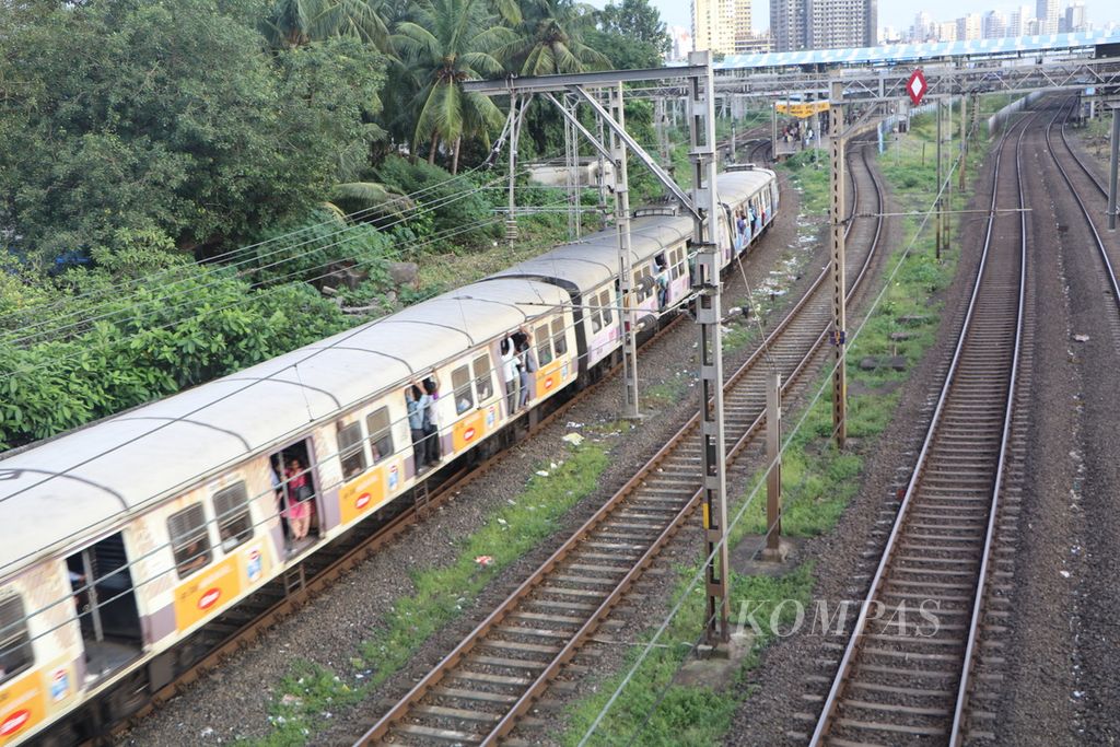 Para penumpang bergantung di pintu kereta rel listrik yang terbuka di kota Mumbai, India, Selasa (26/9/2023). 