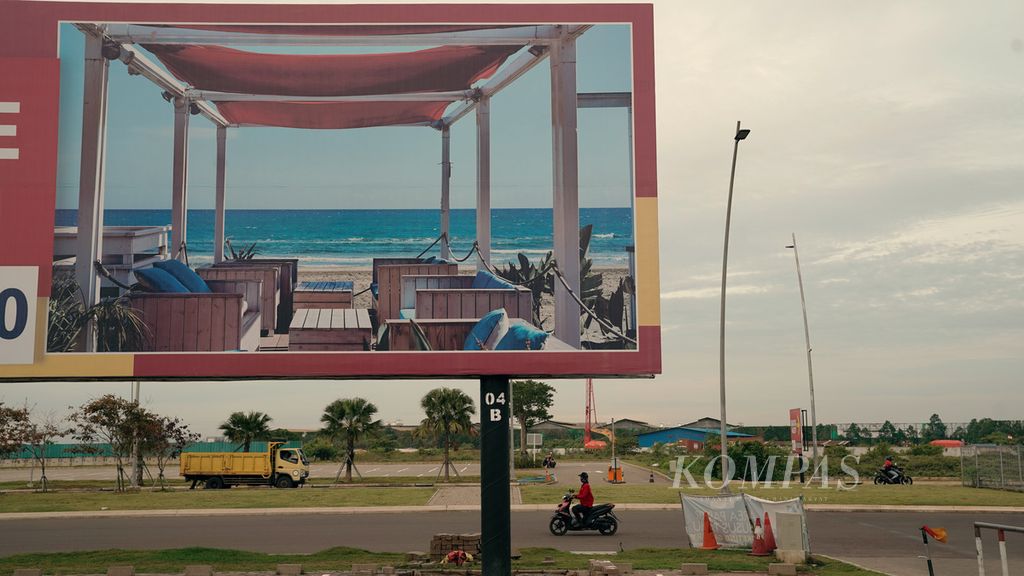 Warga melintasi baliho iklan kafe yang akan segera berdiri di Pantai Pasir Putih PIK 2 di Kelurahan Dadap, Kecamatan Kosambi, Tangerang, Banten, Sabtu (8/10/2022). Hasil reklamasi Teluk Jakarta tersebut dulunya dikenal dengan nama Pulau C. 
