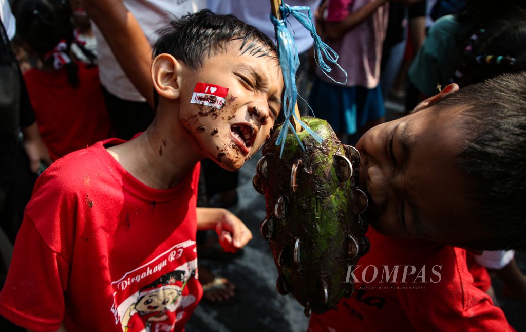 Anak-anak dengan gigih mencabut koin di buah pepaya dengan menggunakan gigi dalam rangka menyemarakkan HUT Ke-78  Kemerdekaan RI di bantaran Kali Banjir Kanal Barat, Petamburan, Tanah Abang, Jakarta Pusat, Kamis (17/8/2023). 