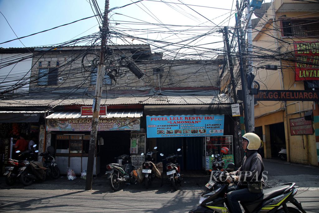 Kabel utilitas yang terlihat semrawut di Jalan KH Syahdan, Palmerah, Jakarta Barat, Selasa (1/8/2023). Keberadaan kabel yang semrawut, tumpang tindih, menjuntai, dan menonjol di jalanan tidak hanya tidak enak dipandang, tetapi juga membahayakan pengguna jalan. 