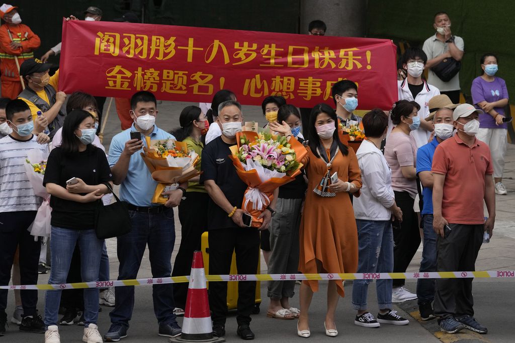 Anggota keluarga siswa memegang bunga dan membentangkan spanduk ucapan selamat pada hari terakhir ujian masuk perguruan tinggi nasional, yang dikenal sebagai gaokao, di Beijing, Jumat, 10 Juni 2022. Lebih dari 11 juta siswa SMA di seluruh China mengikuti ujian masuk perguruan tinggi tahunan paska pandemi Covid-19. 