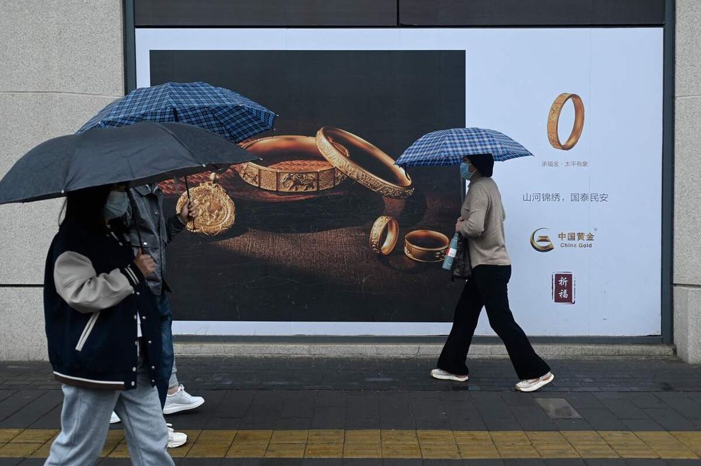 Warga berjalan memegang payung di depan papan iklan penjualan emas di Beijing, China, 10 April 2024. 