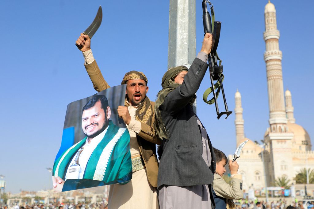 Salah seorang pejuang Houthi memegang potret pemimpin Houthi, Abdul Malik al-Houthi (kiri), sementara rekannya mengacungkan senjata dalam aksi protes menyusul serangan pasukan AS dan Inggris di ibu kota Sana’a, Yaman, pada Jumat (12/1/2024). 