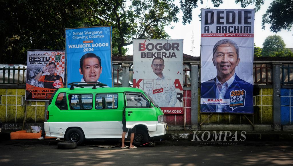 Seorang sopir angkutan kota berusaha memperbaiki kendaraannya di bawah deretan poster bergambar para tokoh yang mencalonkan diri dalam Pemilihan Wali Kota Bogor pada Pilkada 2024 di Jalan Perintis Kemerdekaan, Kota Bogor, Jawa Barat, Minggu (19/5/2024). 