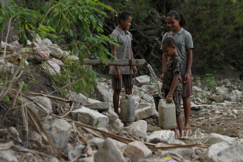 Esra Notunis (14) bersama dua adiknya, Ferni (12) dan Miki Nitboho (7), memperagakan proses pengambilan air bersih dari mata air tak jauh dari Sungai Noefatu, Desa Falas, Kecamatan Kie, Kabupaten Timor Tengah Selatan, Nusa Tenggara Timur, Senin (30/5/2022).
