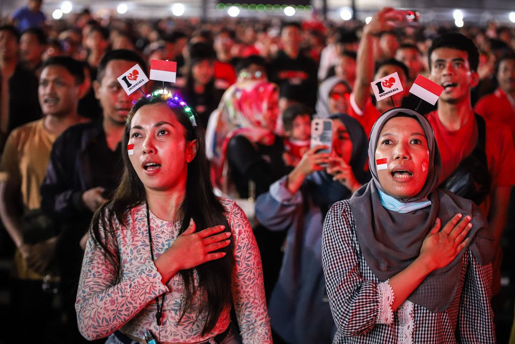 Warga menyanyikan lagu ”Indonesia Raya” saat menyaksikan pertandingan timnas Indonesia melawan Australia pada laga kualifikasi Piala Dunia 2026 putaran ketiga Zona Asia di Surabaya Expo Center, Surabaya, Jawa Timur, Selasa (10/9/2024).