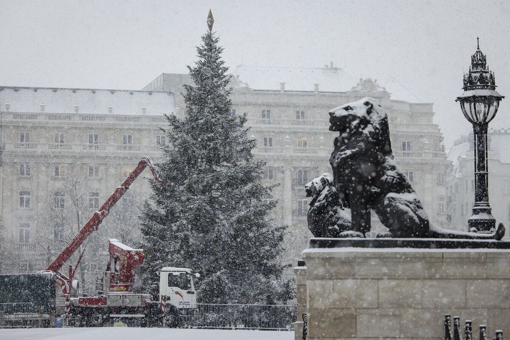 Para pekerja menghias pohon Natal di tengah hujan salju lebat di alun-alun Kossuth di gedung parlemen di Budapest, Hongaria, Kamis (30/11/2023). 