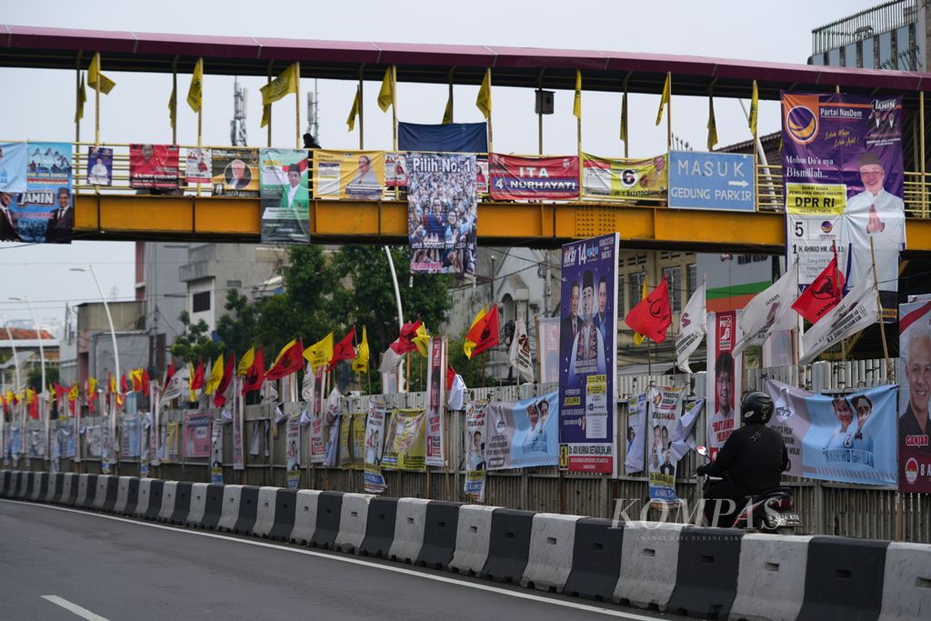 Pengendara melintasi bendera partai politik peserta Pemilu 2024 dan calon legislatif yang dipasang di sekitar Pasar Jatinegara, Jakarta Timur, Senin (1/1/2024). Masa kampanye digunakan partai politik untuk memasang alat peraga kampanye. Biaya politik yang mahal dinilai telah menjadi salah satu penyumbang kemunduran demokrasi. 