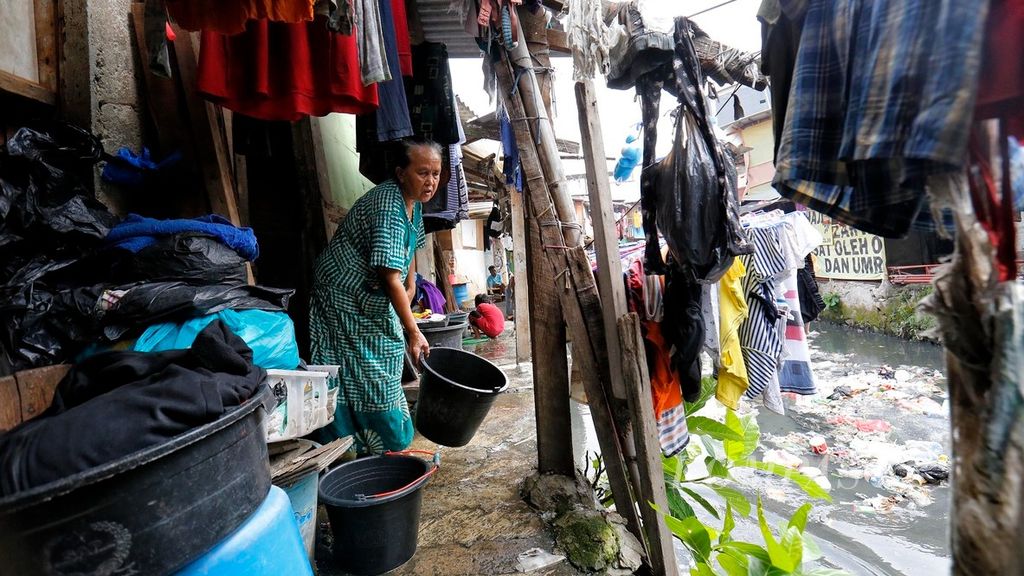 Rohmah mencuci pakaian di depan rumahnya yang berada di kawasan permukiman padat yang sebagian besar dihuni warga miskin, di tepian terusan Sungai Krukut, kawasan Kebon Kacang, Jakarta Pusat, Selasa (30/5/2022). 