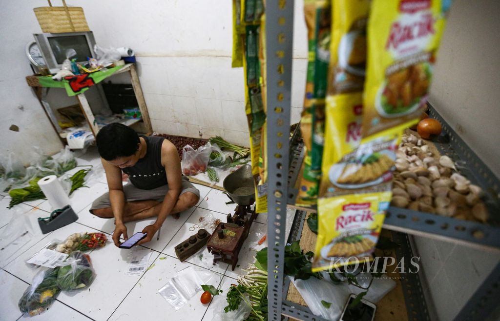 Pedagang memeriksa pesanan pelanggan melalui telepon seluler di sebuah rumah petak di kawasan padat di Tegal Parang, Mampang Prapatan, Jakarta Selatan, Senin (21/2/2022). Karena terimbas pandemi Covid-19, sejak dua tahun lalu para pedagang sayur keliling ini mulai berjualan sayur mayur melalui lokapasar atau marketpalce seperti Tokopedia, Lazada, dan Shopee. Pedagang mengakui, melalui lokapasar mereka dapat menembus pelanggan di kawasan elit dan apartemen yang selama ini tidak dapat dijangkau.