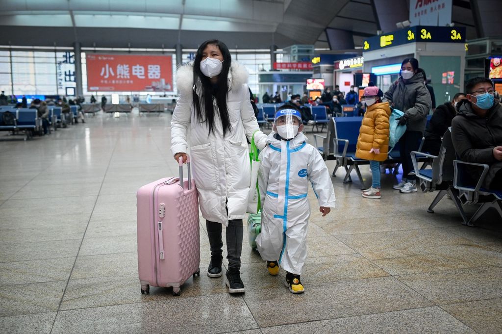 Seorang perempuan menuntun anaknya yang mengenakan alat pelindung diri saat berjalan di stasiun kereta di Beijing, 12 Januari 2023, saat dimulainya musim mudik untuk perayaan Imlek. 