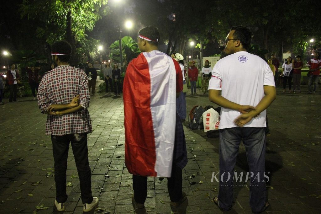 Seorang peserta aksi solidaritas untuk korban bom di Surabaya, yang diselenggarakan di Taman Suropati, Jakarta, Minggu (13/5/2018) malam, membawa bendera Merah Putih. Mereka berharap agar masyarakat Indonesia tetap bersatu melawan terorisme.