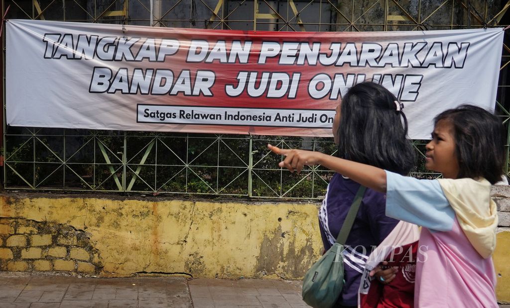 Warga melintasi spanduk berisikan tuntutan pemberantasan judi daring yang terpasang di salah satu sudut kawasan Pasar Senen, Jakarta, Minggu (4/8/2024). Hingga kini banyak kalangan masyarakat masih menanti keseriusan, keberanian, dan aksi nyata pemerintah menindak para penggerak dan bandar judi daring. 