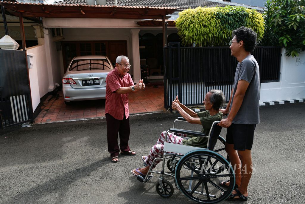 Sri Warso Wahono (74) duduk di kursi roda menyapa para tetangganya saat berkeliling kompleks setiap pagi bersama putranya, Aria, di kawasan Palmerah, Jakarta Barat, Rabu (25/5/2022). Selain dapat menikmati matahari pagi, Pak Warso juga dapat bersosialisasi dengan para tetanggannya yang sebagian besar juga sudah lansia.