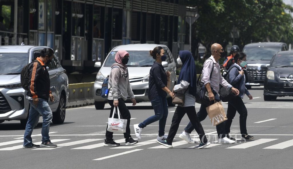 Sejumlah pekerja kantor menyeberang di Jalan Sudirman menuju tempat kerja di kawasan Sudirman, Jakarta, Februari 2022.  