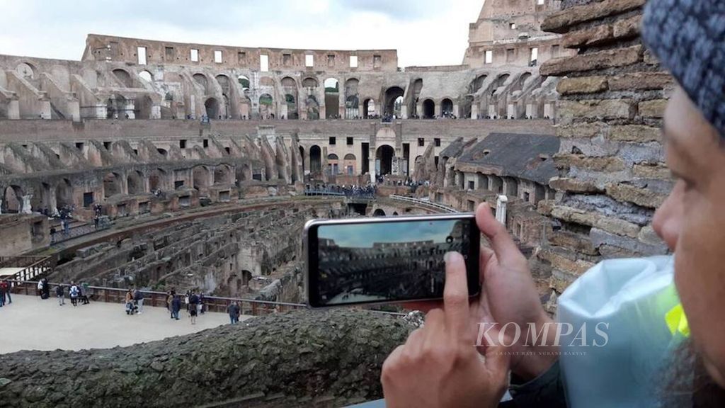 Pengunjung mengabadikan bangunan Colosseum di tengah kota Roma, Italia, dengan menggunakan ponsel, Rabu (7/2/2018).